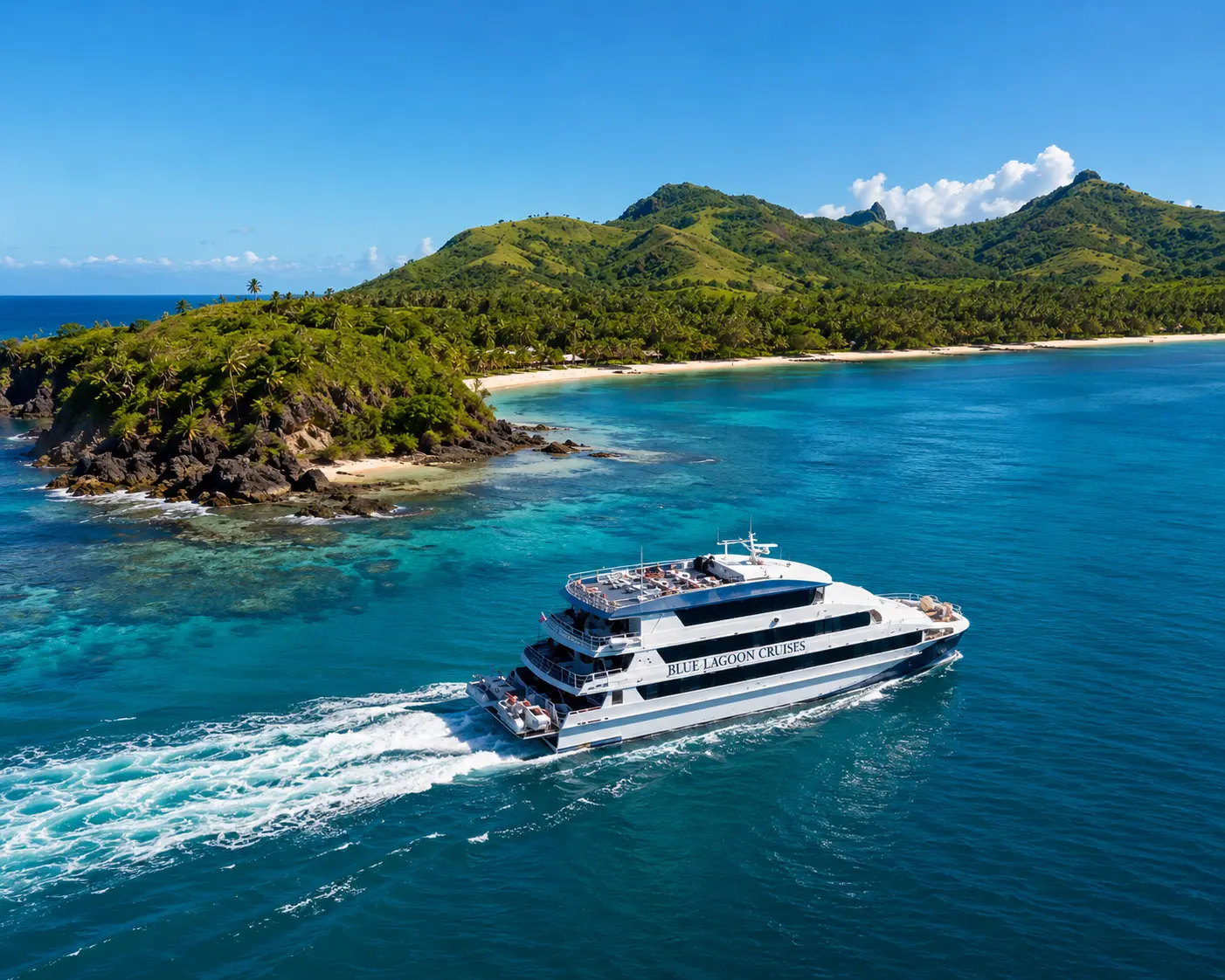 A cruise catamaran passing a green, palm-fringed island in clear turquoise water